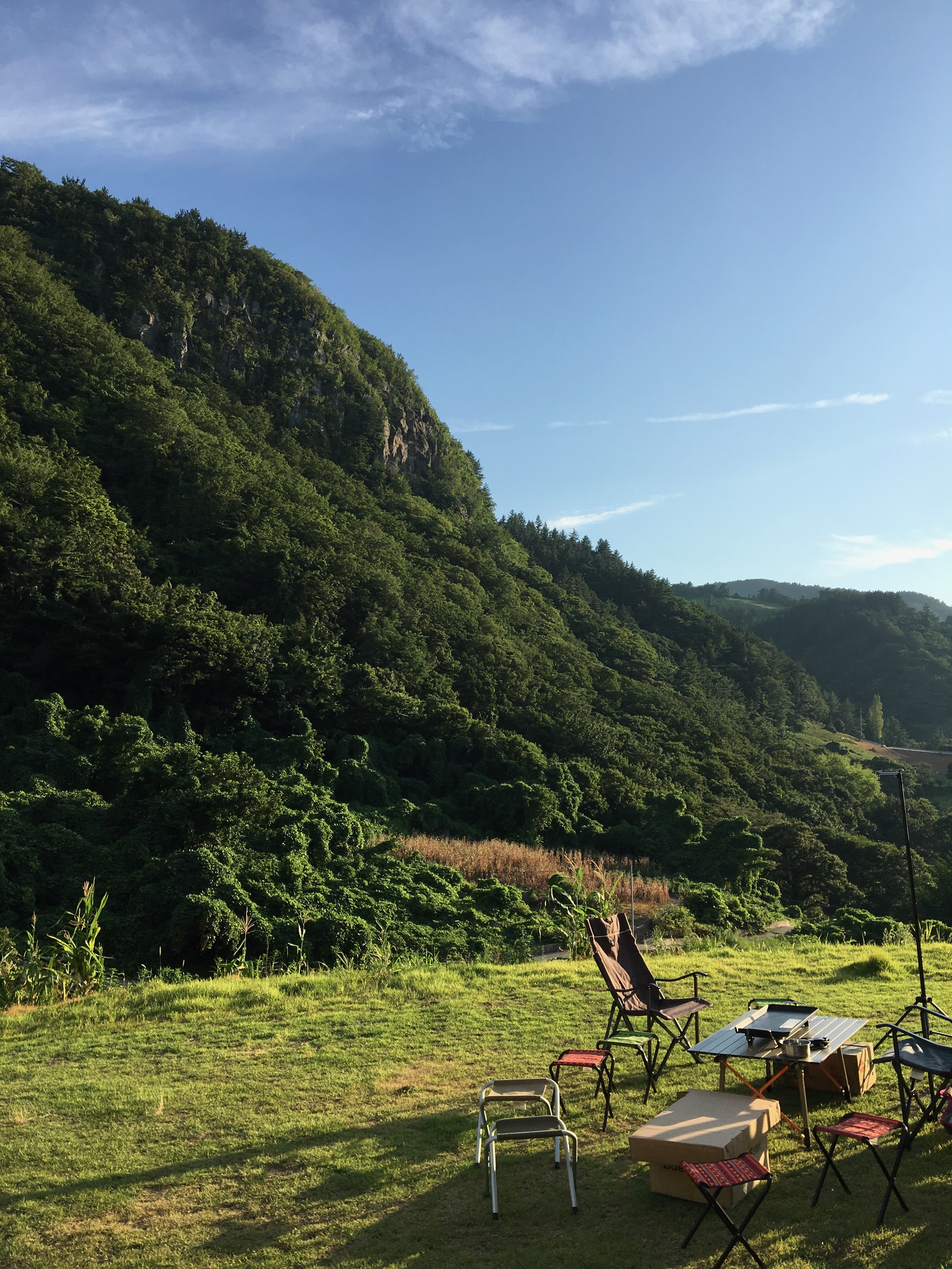 Open grassy landscape with chairs and tables set against a green hillside