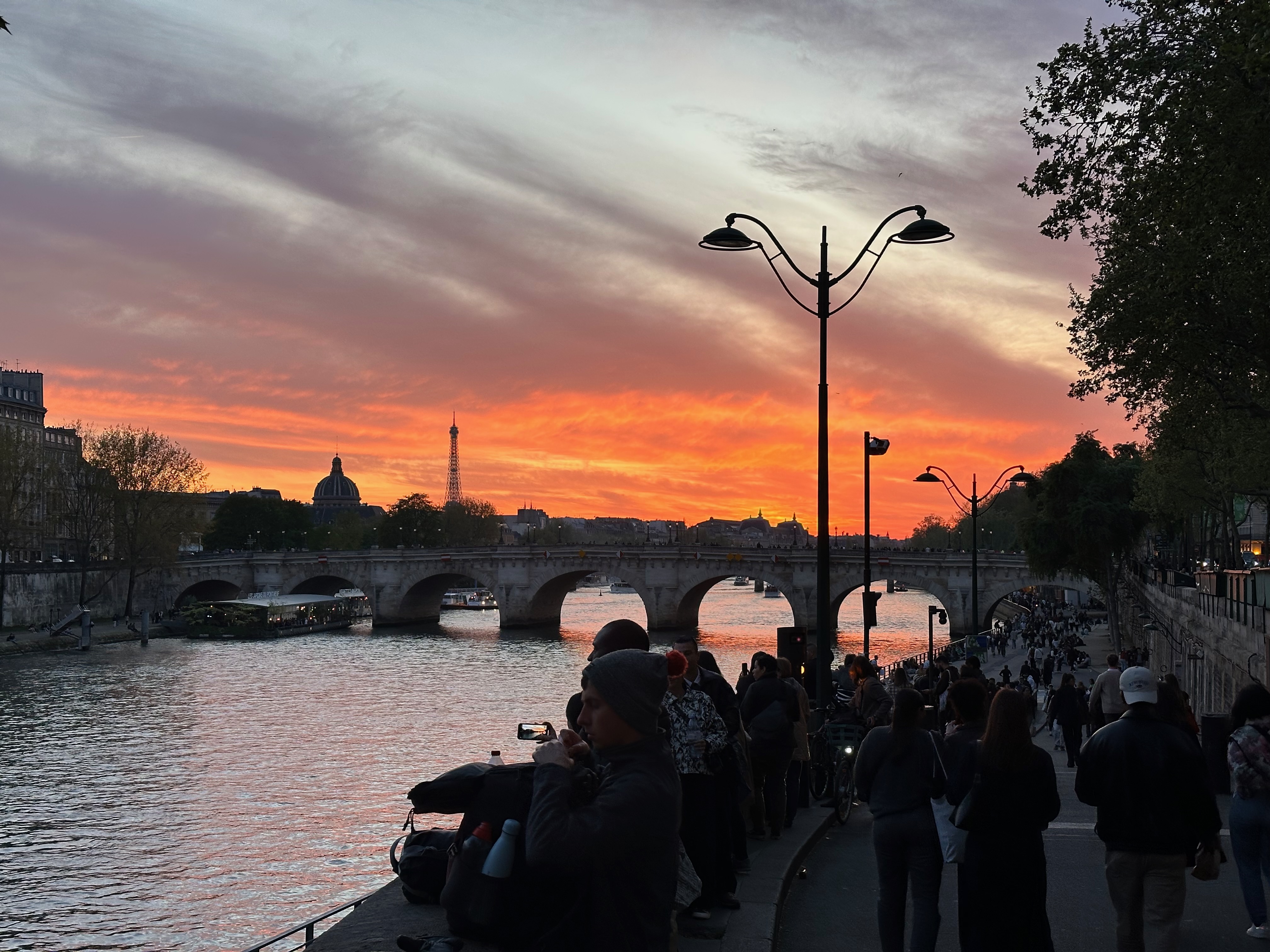 Sunset riverside view with a bridge and people walking along the Seine in Paris
