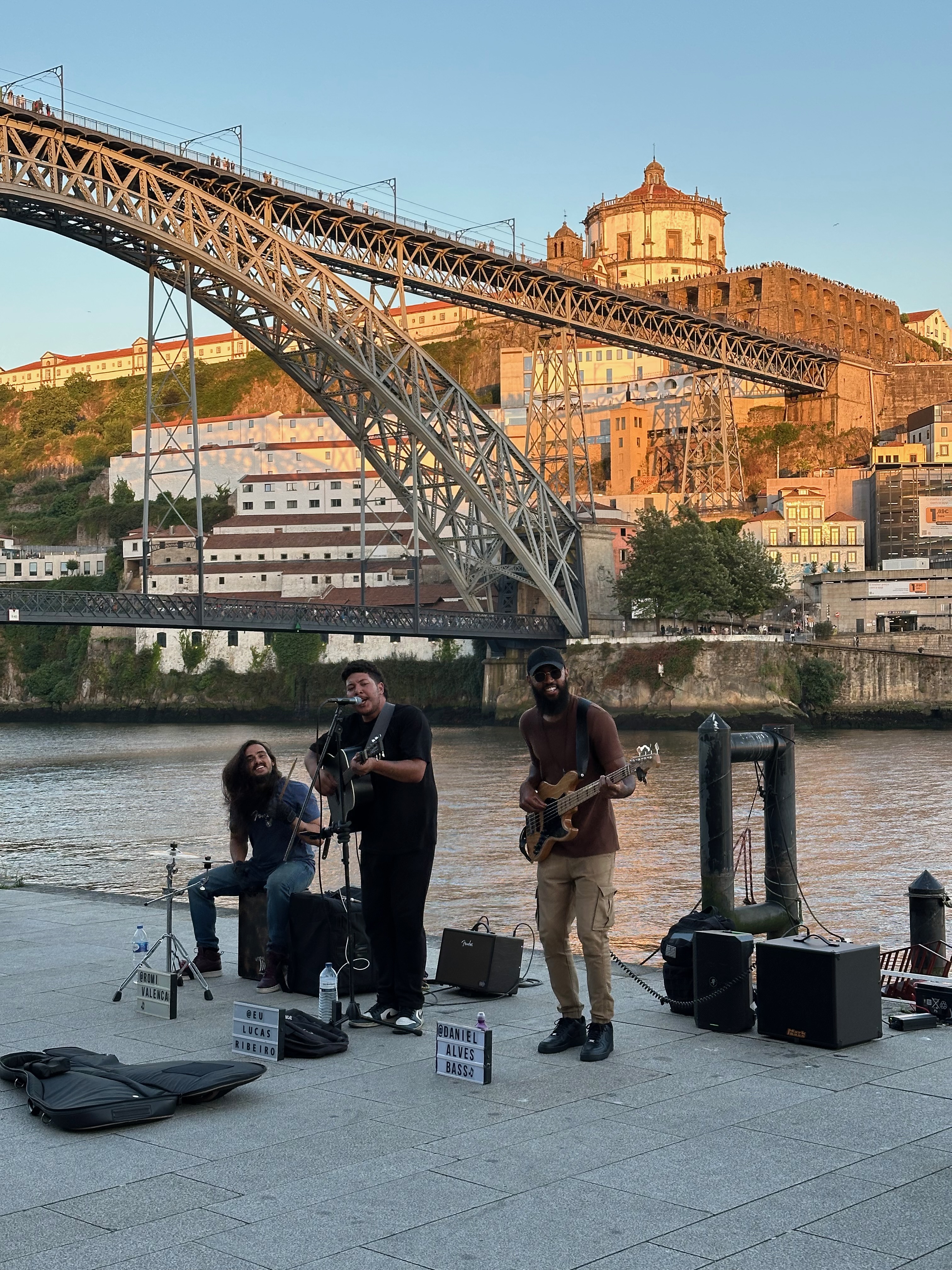 Street musicians performing by the river beneath Dom Luis I Bridge in Porto at sunset